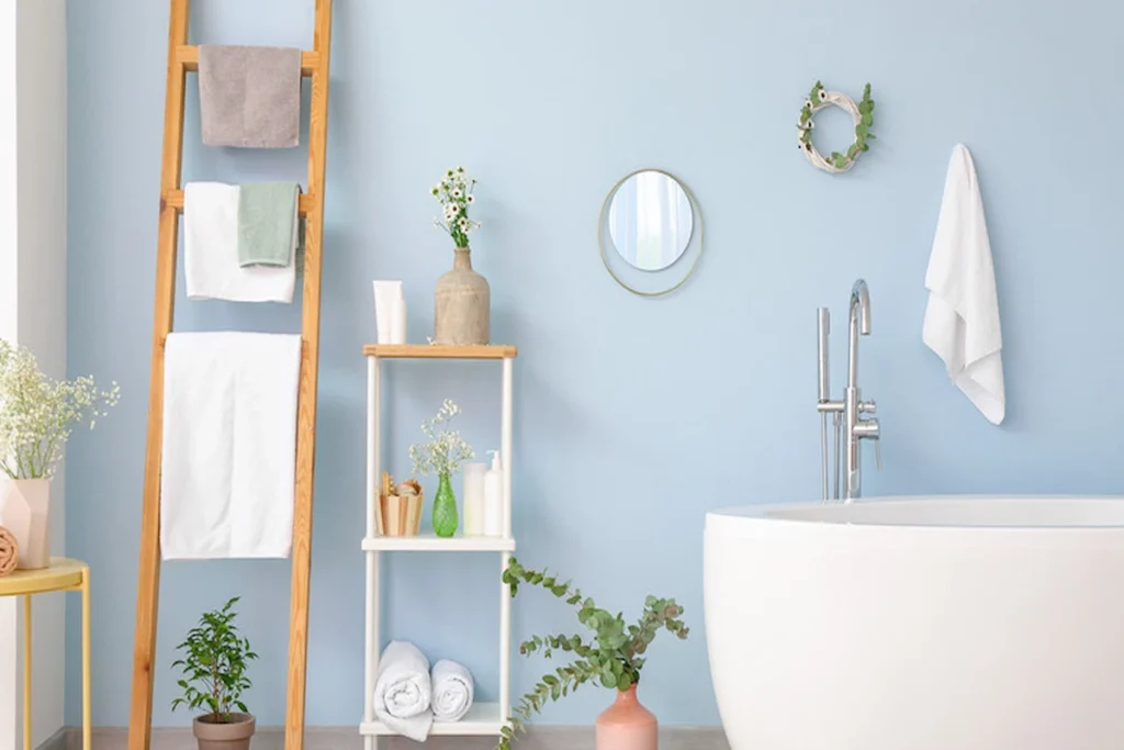 bathroom interior showing a wooden towel ladder and shelving unit on the left, and a freestanding bathtub with wall decor on the right.