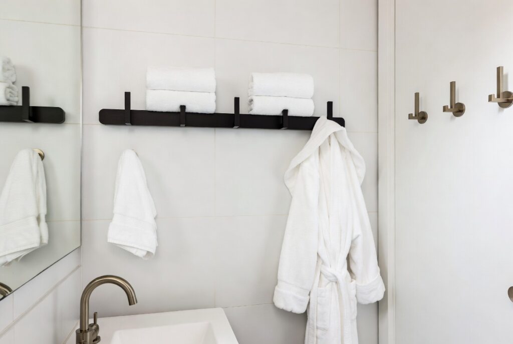 Stylish matte black horizontal hook rail and robe hooks in a modern bathroom, holding towels and bathrobe with proper spacing for fast drying.